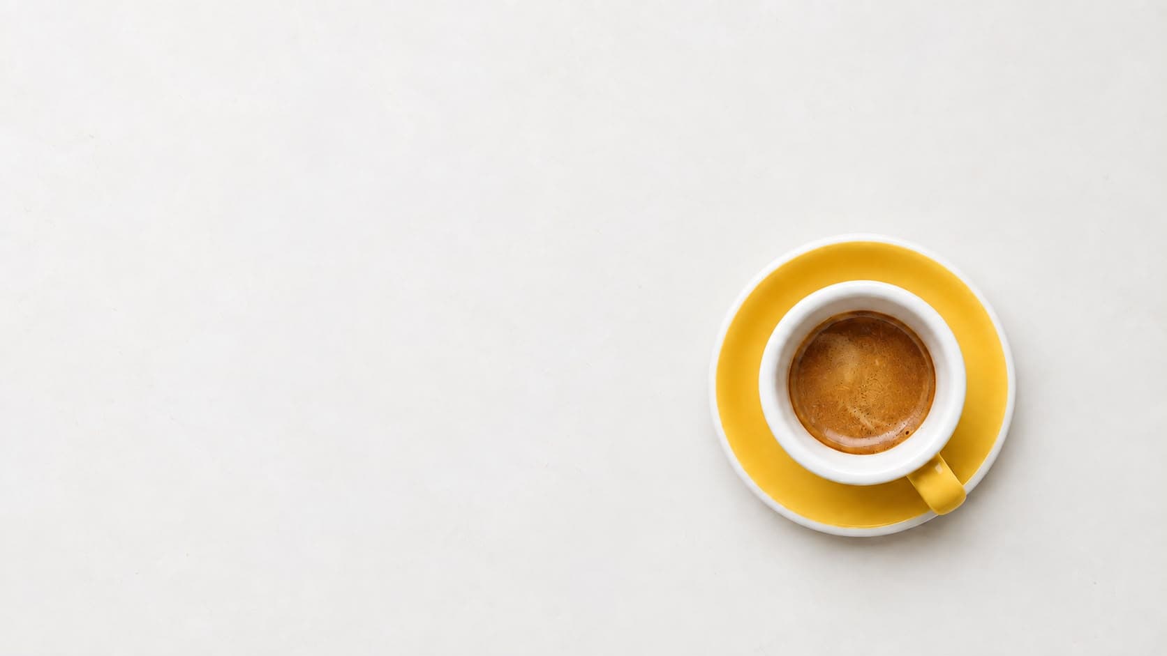 Espresso in a yellow-saucered cup on a white surface